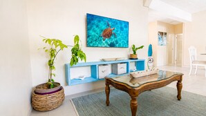 A living room with a wooden coffee table, a blue console table with storage, a large painting of a turtle, and potted plants. - Charming 2-bedroom Apartment with AC at gorgeous Crane Beach (Bridgetown)