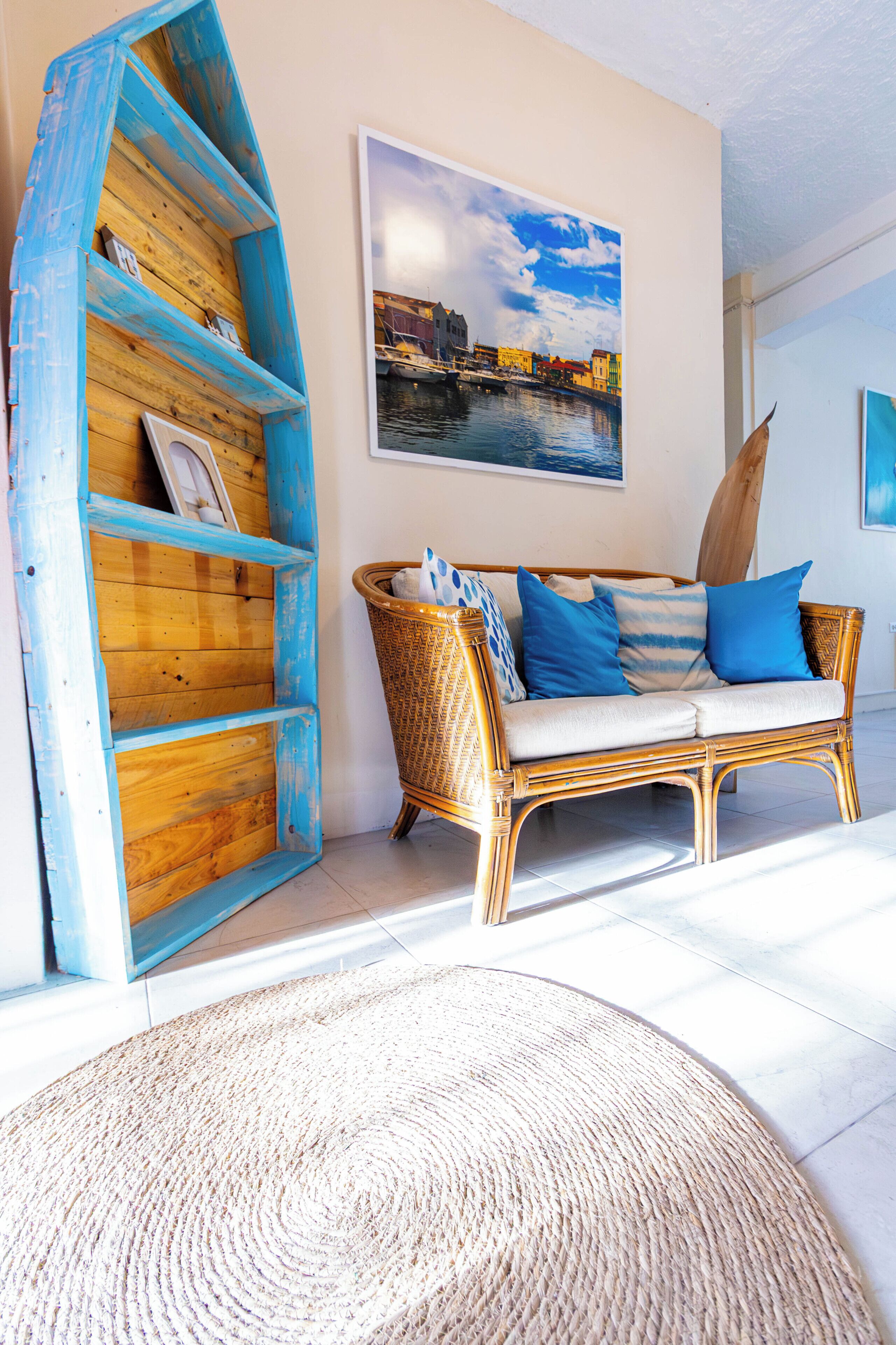 A room with a wicker sofa, a blue-painted wooden shelf, and a woven rug.