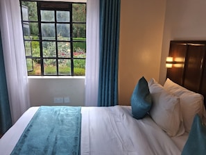 A hotel room with a bed, a window with curtains, and a nightstand with a lamp. - Riata Loltome (Nyahururu)