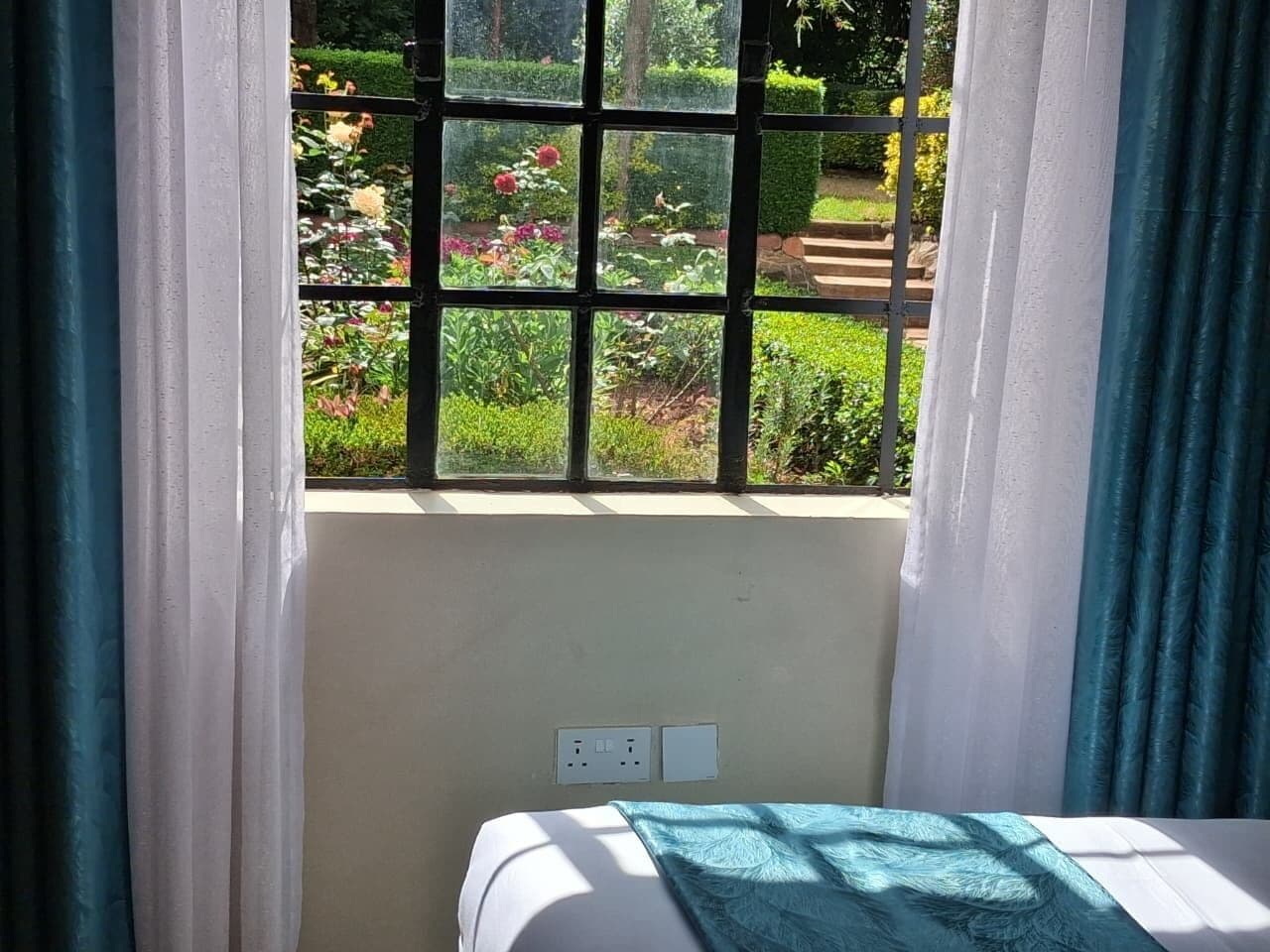 Quarto com cama, janela vista para um jardim e tomada na parede.