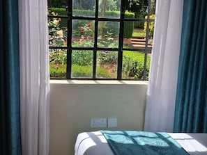 A room with a bed, a window with a view of a garden, and a power outlet on the wall. - Riata Loltome (Nyahururu)
