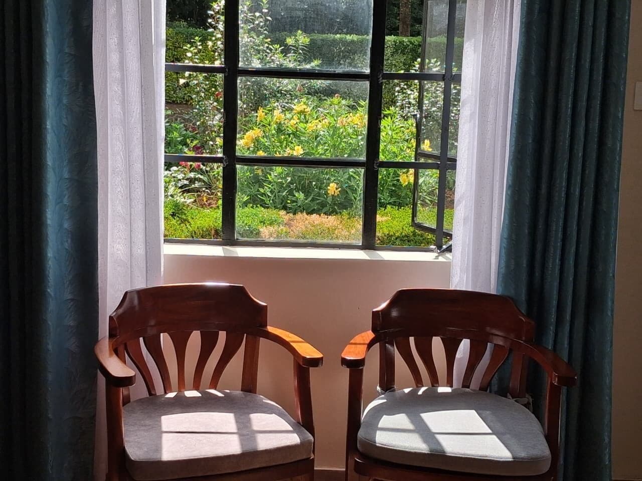 Duas cadeiras de madeira viradas para uma janela com vista para um jardim.