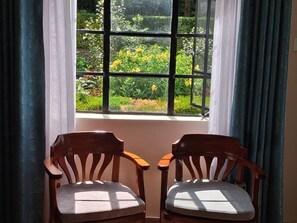 Dos sillas de madera orientadas hacia una ventana con vistas a un jardín.