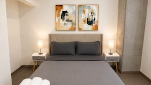 Een hotelkamer met een groot bed, twee nachtkastjes met lampen, abstracte kunst aan de muur en een opgerolde handdoek op het bed.