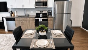 Een moderne keuken met roestvrijstalen apparatuur, een eettafel gedekt voor vier personen en een kleine potplant.