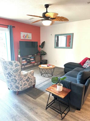 Ein Wohnzimmer mit Deckenventilator, einer Couch, einem Couchtisch, einem Fernseher und einer Pflanze.