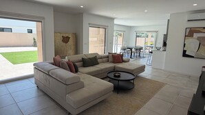 A modern living room with a sectional sofa, a coffee table, and a dining area with a table and chairs. - Vila d'Arrabida (Quinta do Anjo)