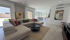 A modern living room with a sectional sofa, a round coffee table, and a kitchen area visible through an open sliding door. - Vila d'Arrabida (Quinta do Anjo)