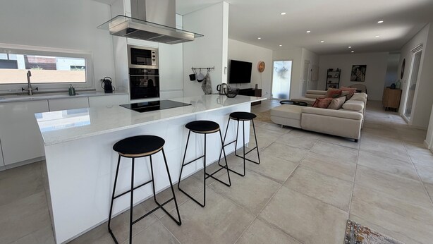 A modern kitchen with a central island, bar stools, a built-in oven, and a large window. - Vila d'Arrabida (Quinta do Anjo)