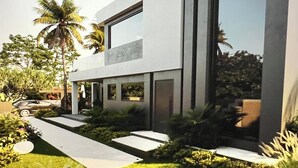 Ein modernes, zweistöckiges Haus mit großen Fenstern, einem gepflegten Garten und einer Palme.