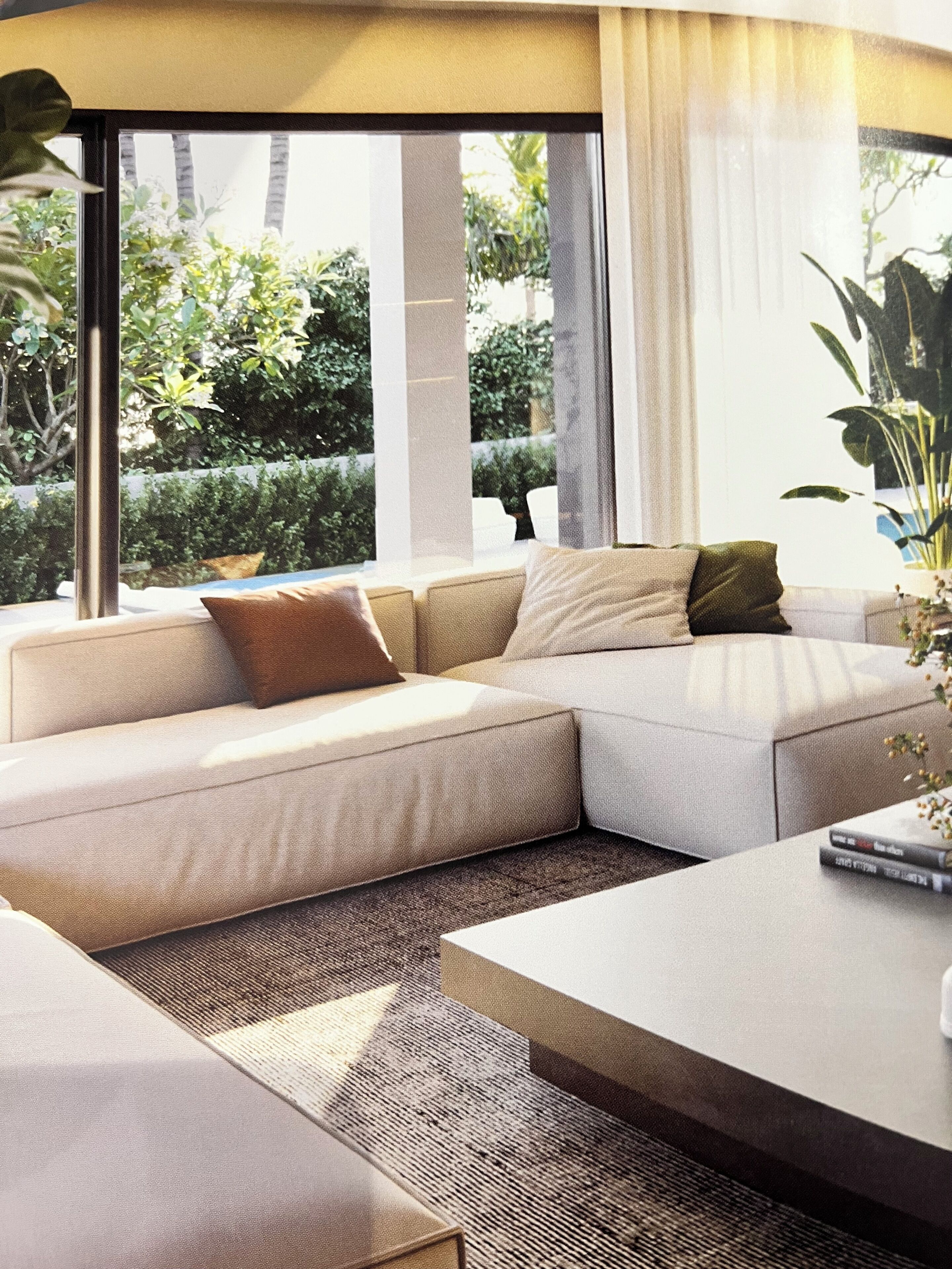 Un salon moderne avec un canapé d’angle, une table basse et de grandes fenêtres donnant sur un paysage verdoyant.