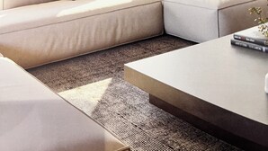 Ein modernes Wohnzimmer mit einer Eckcouch, einem Couchtisch und großen Fenstern mit Blick auf Grünflächen.