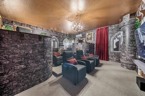 Ein Zimmer mit Stehwänden, einem Chandelier und mehreren Sesseln mit roten Kissen.