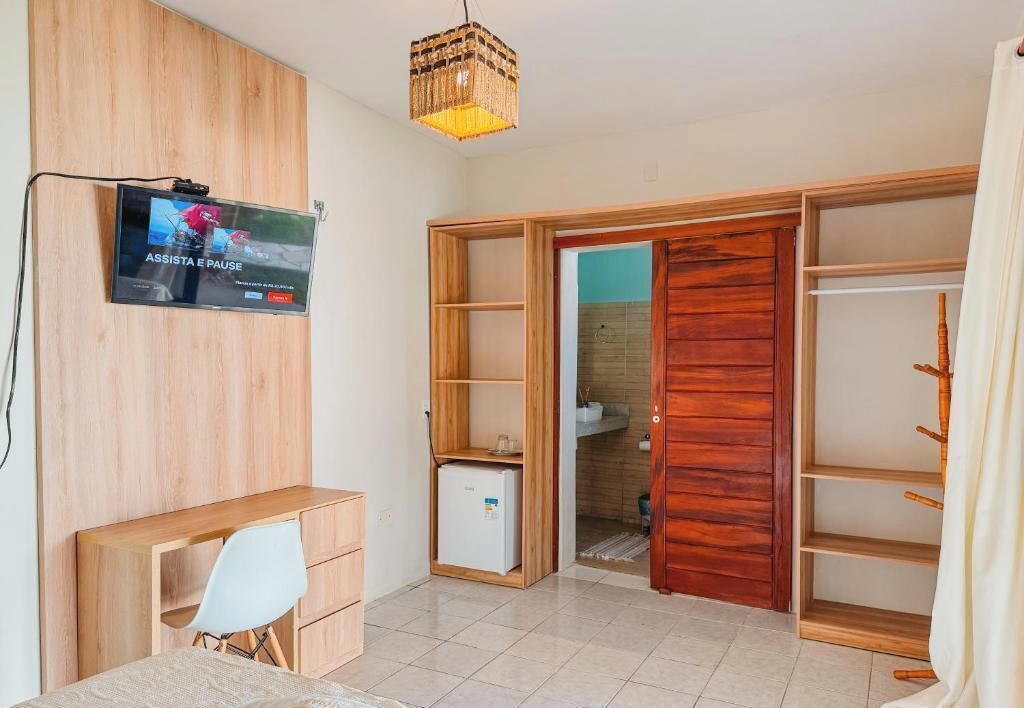 Una habitación con escritorio de madera, televisor montado en la pared y armario con espejo.