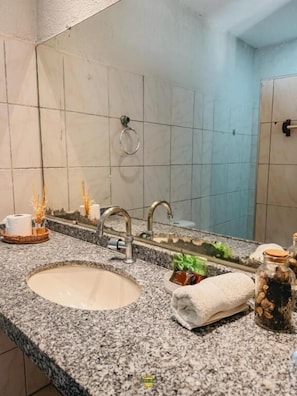 Un baño con encimera de granito, lavamanos, espejo y toallero.