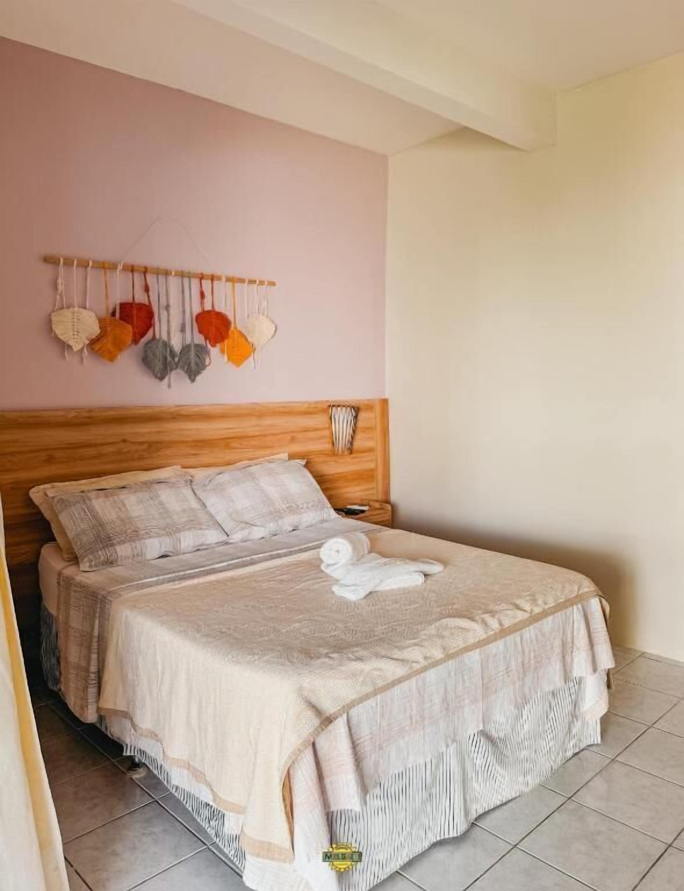 A neatly made bed with a white towel, a wooden headboard, and a wall-mounted macrame decoration.