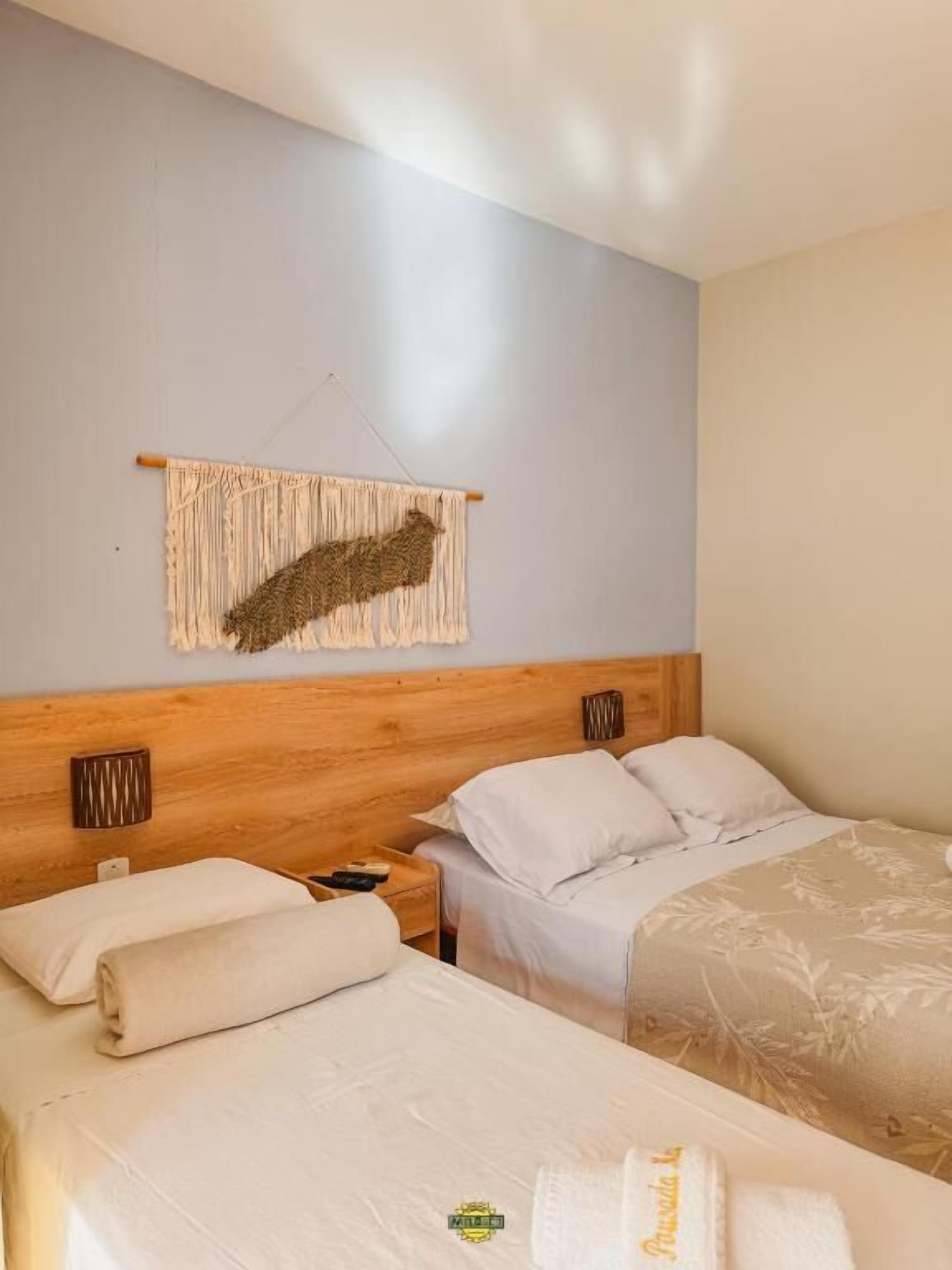 Habitación de hotel con dos camas, cabecero de madera, un tapiz en la pared y una mesita de noche con lámpara.
