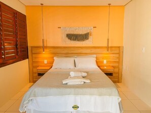 A hotel room with a bed, wooden headboard, two bedside tables, a wall-mounted macrame piece, and a wooden door.