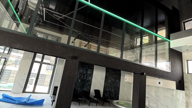 Una piscina interior moderna con techo de cristal, sillas negras y un flotador azul inflable.