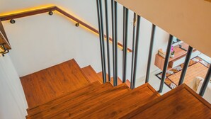 Un escalier en bois avec des rampes en métal mène à une pièce où se trouve un tapis à motifs.