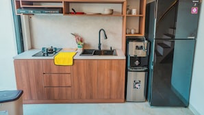 Une cuisine compacte dotée d’une machine à café intégrée, d’un réfrigérateur noir et de meubles de rangement en bois.