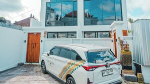 Une maison moderne à deux étages, avec une façade blanche, de grandes fenêtres et une voiture garée dans l’allée.