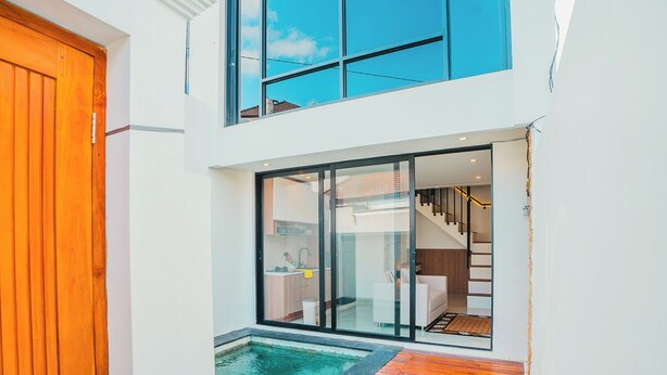 Une maison moderne dotée d’une porte en verre donnant sur un espace de vie, une petite piscine et un escalier.