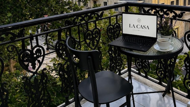 A balcony with a laptop, a chair, and a sign reading 'LA CASA' against a backdrop of a building with multiple windows and balconies. - La Casa Boutique Nizami (Baku)