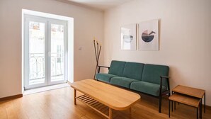 Ein Wohnzimmer mit einem grünen Sofa, einem Holztisch, einem kleinen Beistelltisch und einem Balkon mit Geländer.