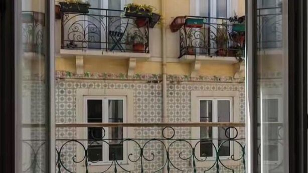 Ein Balkon mit schmiedeeisernen Geländern, Blumentöpfen und Blick auf ein Gebäude mit gemusterten Kacheln und Fenstern.