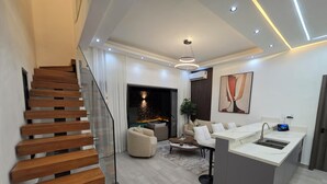Interior moderno com escada, sala de estar com lareira, área de jantar e cozinha com ilha integrada.