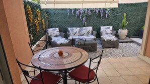 An outdoor patio with wicker furniture, a tiled table, and a decorative wall with hanging flowers. - 2 minutes from the beach: Charming apartment with outdoor space and secure parking (Antibes)