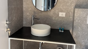 Un baño con un espejo redondo, un lavabo, un perchero para toallas y un inodoro.