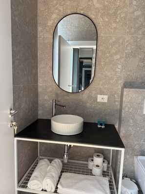 Een badkamer met een ronde spiegel, een wastafel, een handdoekhouder en een toilet.