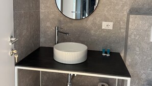 Un baño con un espejo redondo, un lavabo, un perchero para toallas y un inodoro.