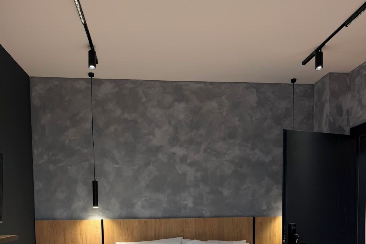 Een moderne slaapkamer met een houten bedframe, een nachtkastje met een lamp en een donkere deur.