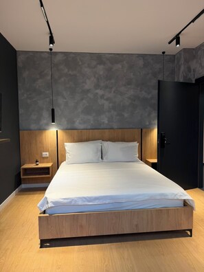 Een moderne slaapkamer met een houten bedframe, een nachtkastje met een lamp en een donkere deur.