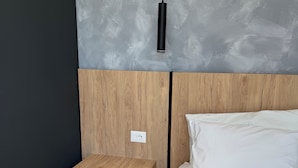 Un dormitorio moderno con cabecera de madera, una mesita de noche, una cama blanca y pared gris con textura.