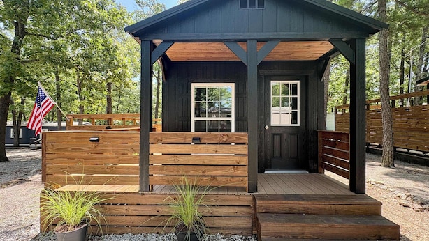 Eine kleine Holzhütte mit Veranda, Tür und Fenstern.