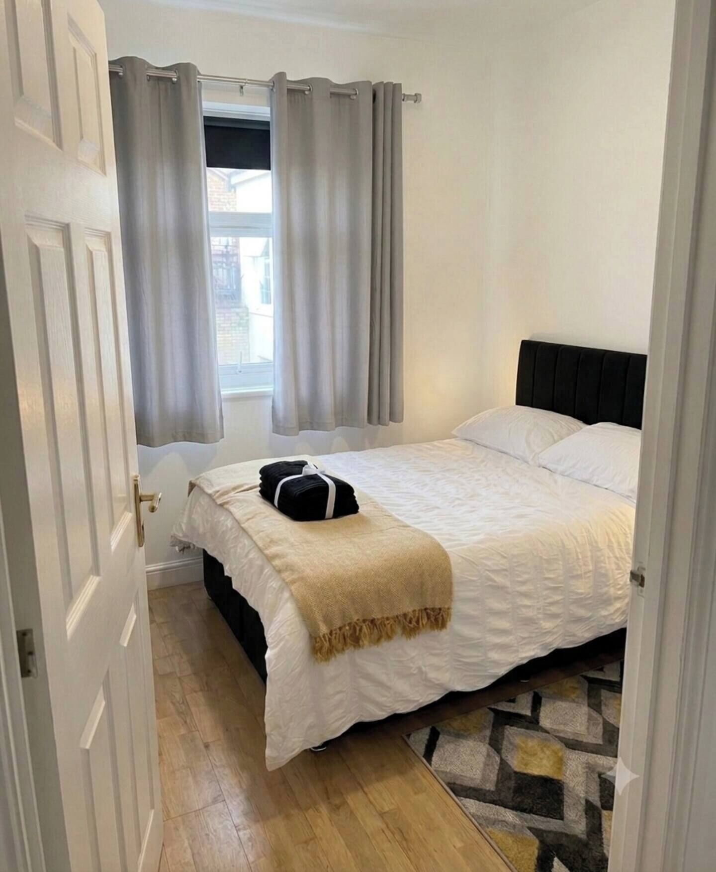 Un dormitorio con cama, ventana con cortinas, puerta y una alfombra estampada.