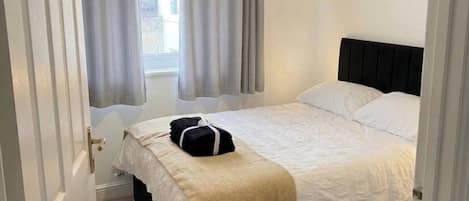 Un dormitorio con cama, ventana con cortinas, puerta y una alfombra estampada.