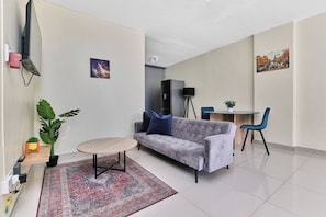 Uma sala de estar moderna com um sofá cinzento, uma mesinha redonda, uma grande planta em vaso e um tapete estampado.