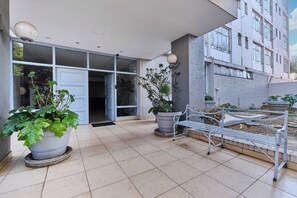 A modern building entrance with a glass door, potted plants, and a metal bench. - Urban Luxe Studio Illovo Mews by ctha (Sandton)