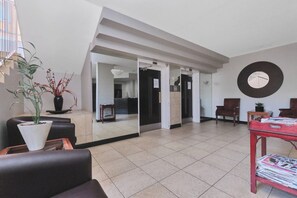 A spacious lobby with a modern design, featuring a seating area with chairs, a coffee table, and a potted plant. - Urban Luxe Studio Illovo Mews by ctha (Sandton)