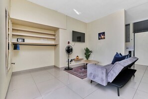 Ein modernes Wohnzimmer mit einer Couch, einem kleinen Tisch, einem Ventilator und einem an der Wand befestigten Fernseher.