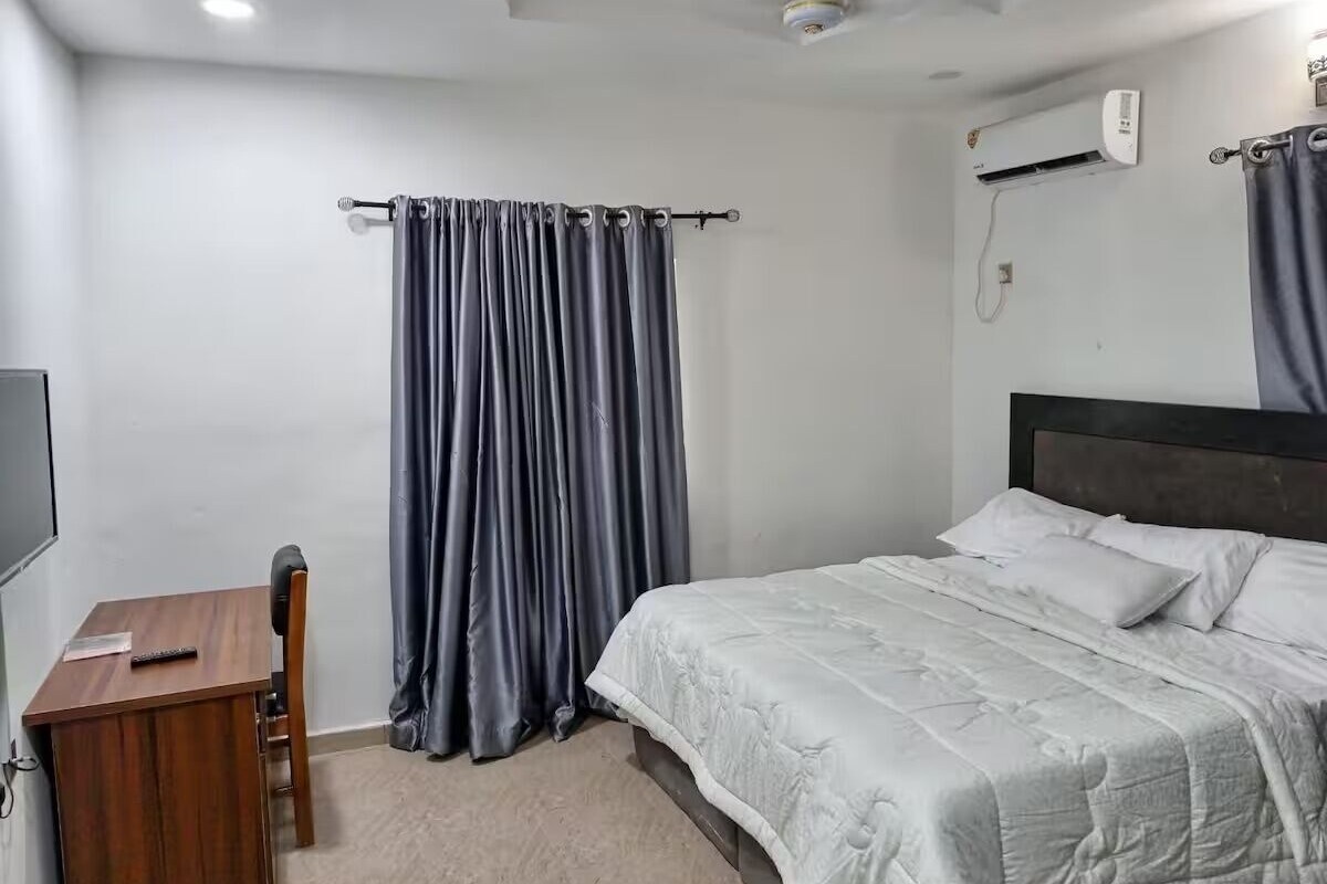 Een slaapkamer met een bed, een bureau, een stoel, een televisie en een raam met gordijnen.