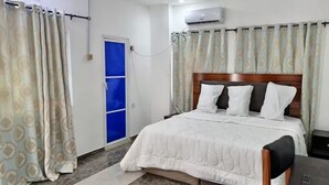 Habitación de hotel con cama, escritorio, silla, ventana con cortinas azules y aire acondicionado.