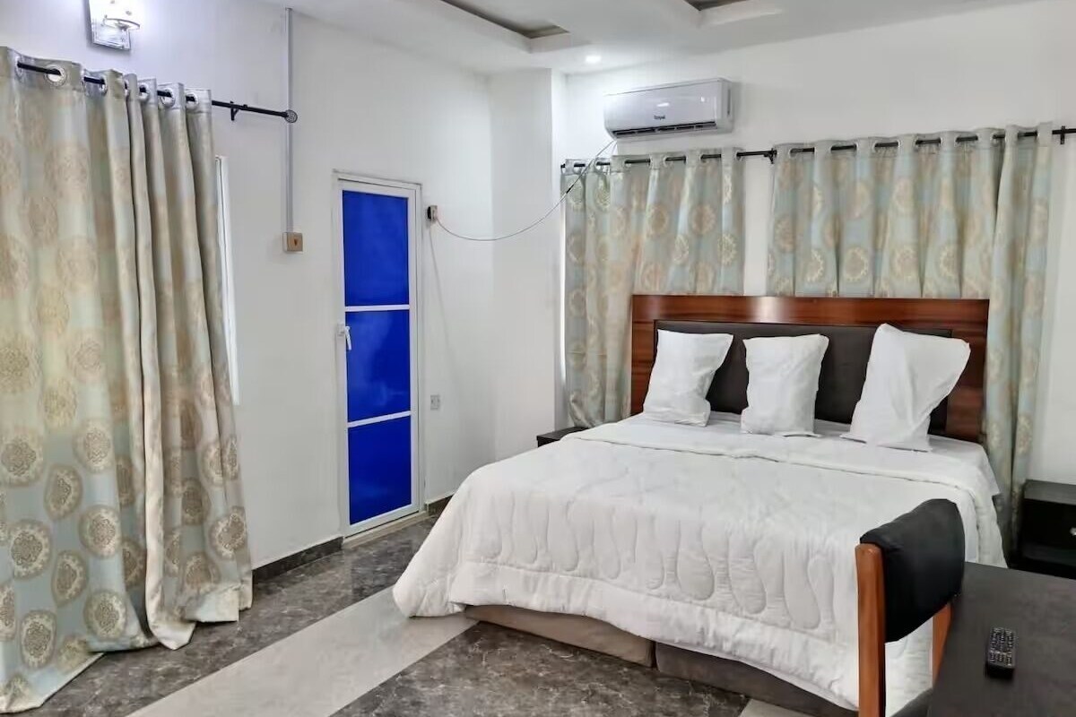 Een hotelkamer met een bed, een bureau, een stoel, een raam met blauwe gordijnen en een airconditioning.