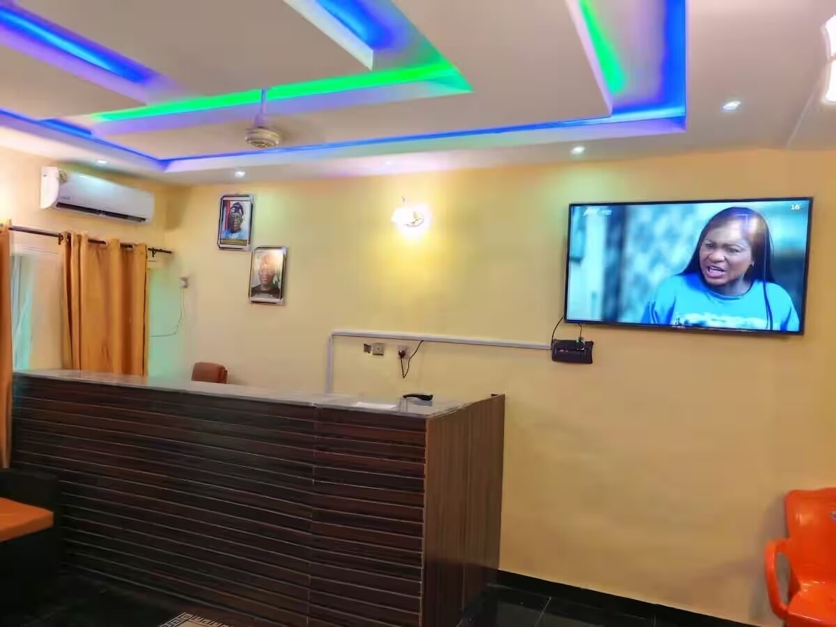 Zona de recepción con un mostrador de madera, un televisor montado en la pared e iluminación azul y verde en el techo.