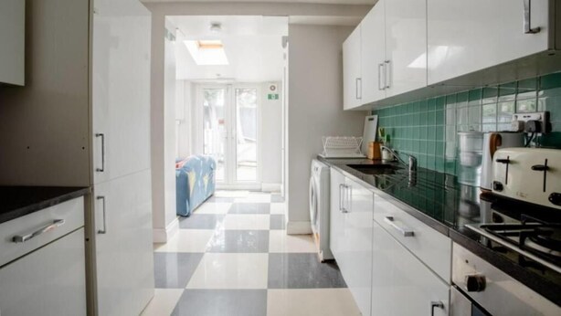 Cocina moderna con armarios blancos, piso a cuadros y vista hacia un cuarto con lavadora.